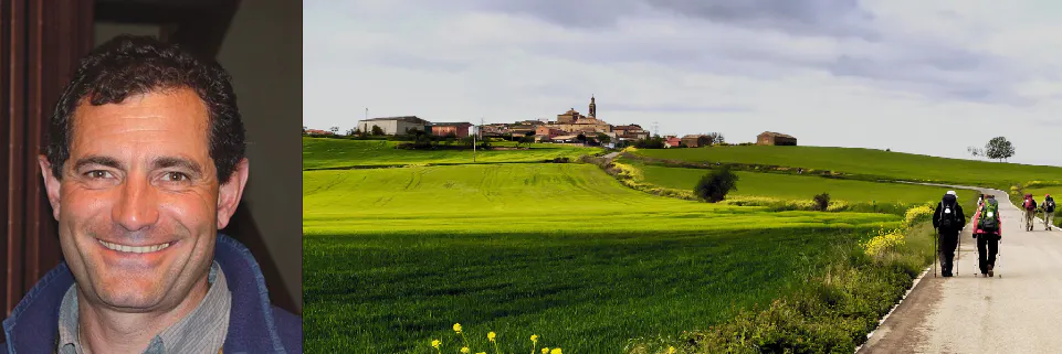 An image of a man walking down a road with a green field in the background.