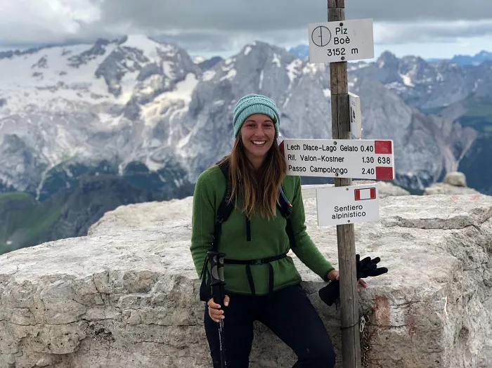 A woman standing next to a sign on top of a mountain.