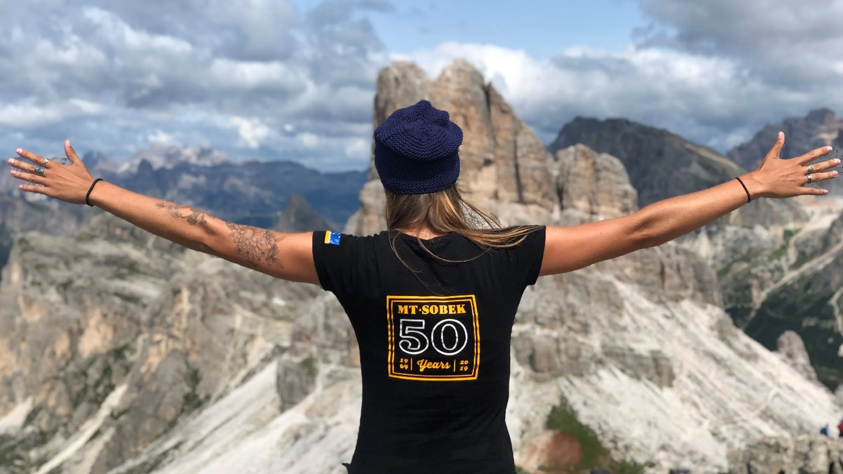 A woman is standing on top of a mountain with her arms outstretched.