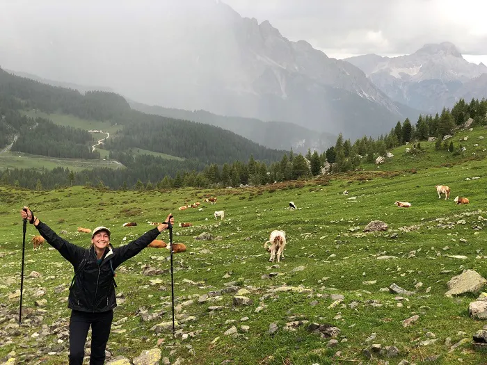 A woman standing in a field with ski poles in front of a herd of cows.