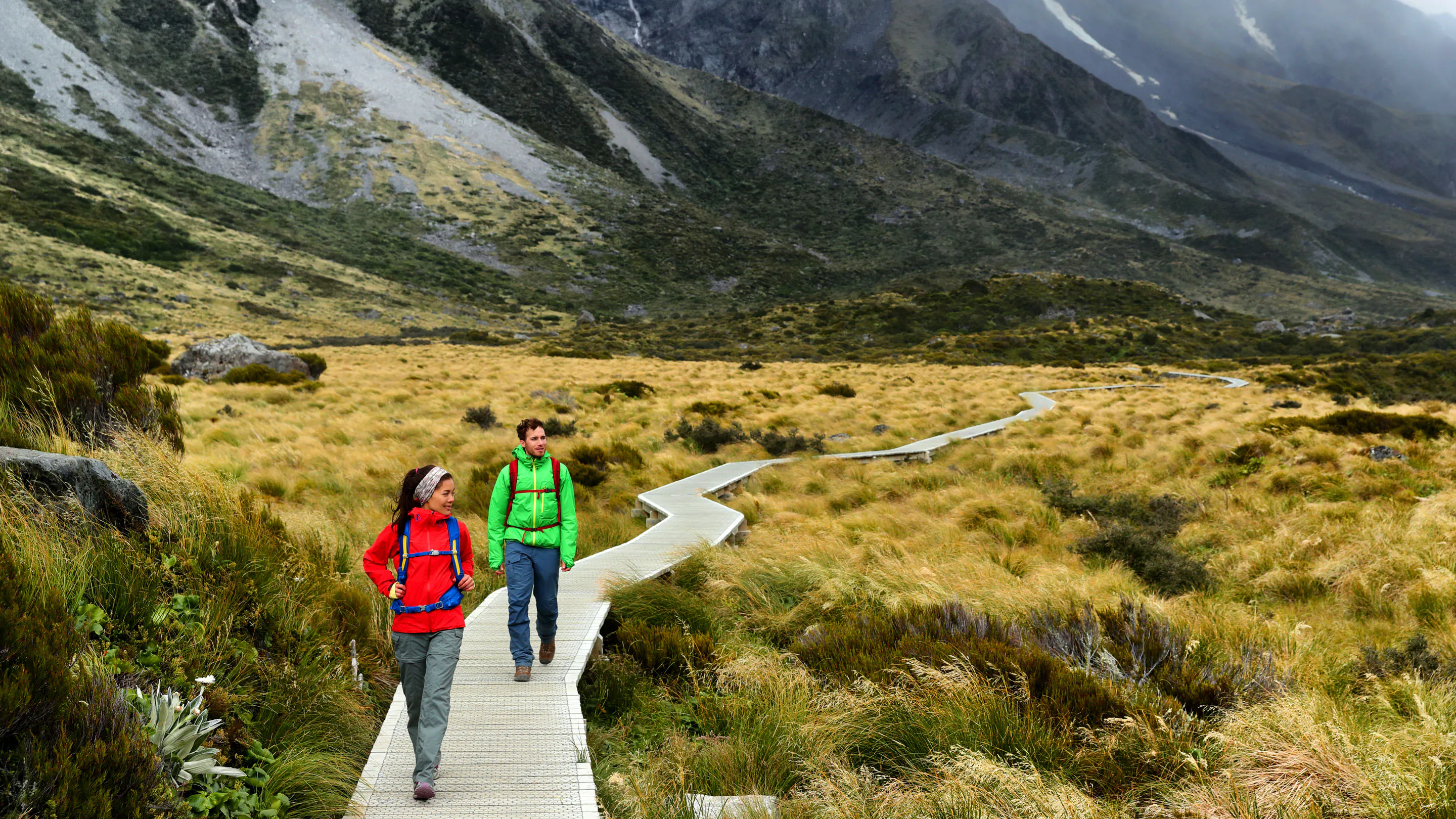 Two travelers male and female walking on a boardwalk in the mountains in New Zealand, Europe