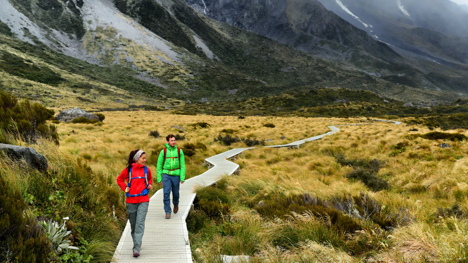Two travelers male and female walking on a boardwalk in the mountains in New Zealand, Europe