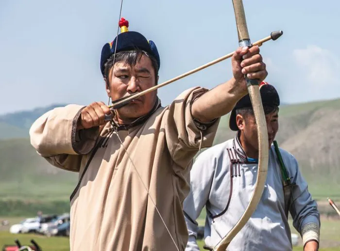 Two men are aiming their bows in a field.