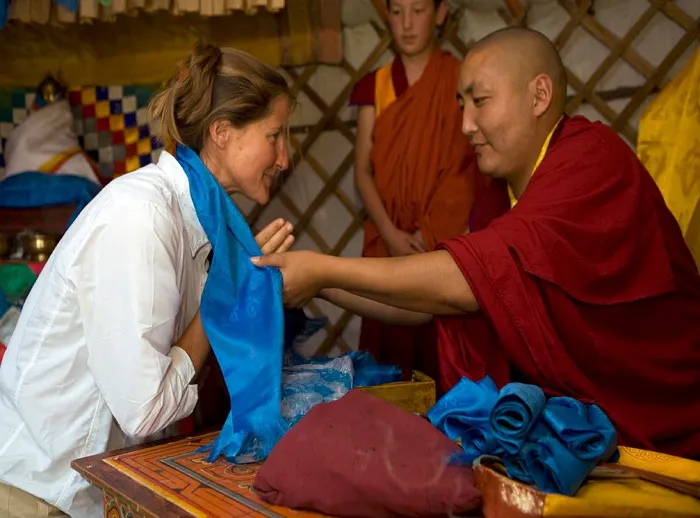 A buddhist monk is putting a blue cloth on a woman's head.