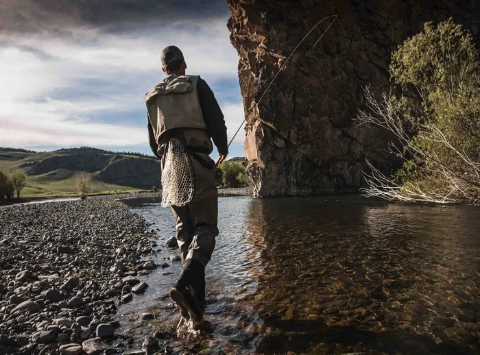 A man is standing in a river near a cliff.