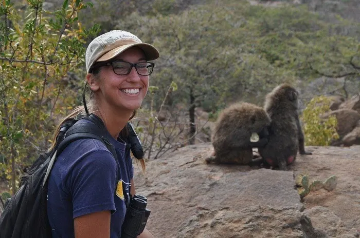 A woman smiles while sitting on a rock with baboons.
