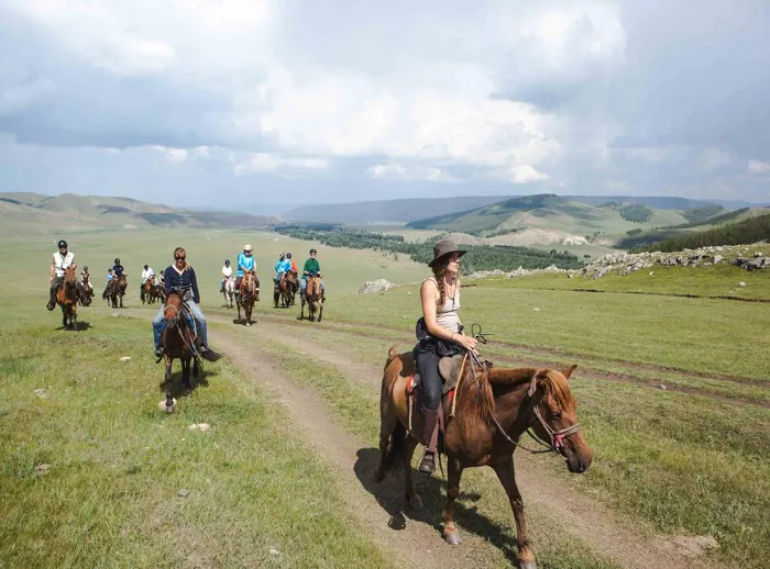 A group of people riding horses through a grassy field.