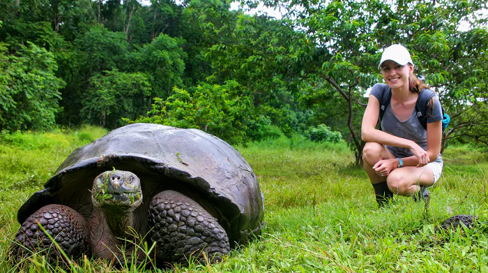 A woman kneeling down next to a giant tortoise.