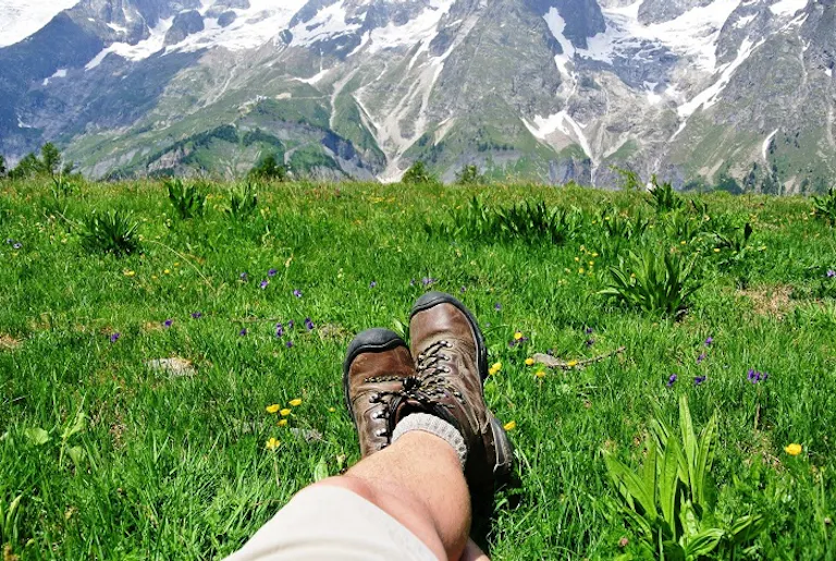 Man with khaki pants and brown boots resting on the green grass on the Alps
