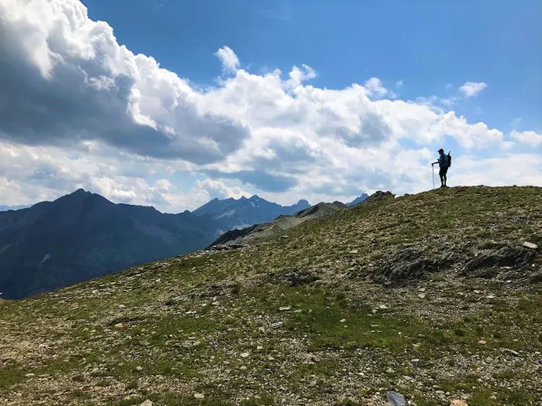 Man with a hiking pole looking at the bottom of the Alps cliff