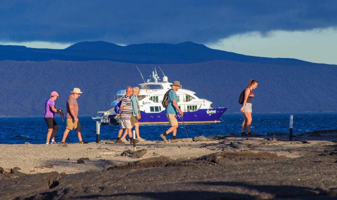 A group of people standing on a beach with a boat in the background.