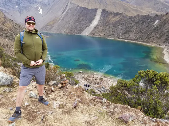 A man standing on top of a mountain next to a lake.