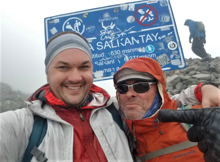 Two men standing in front of a sign at the top of a mountain.