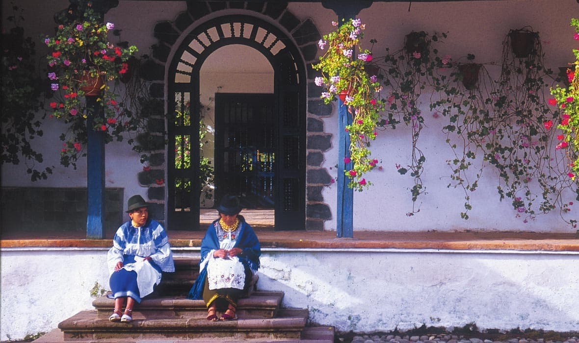 Two women Extend Your Ecuador Trip while sitting on steps in front of a house.