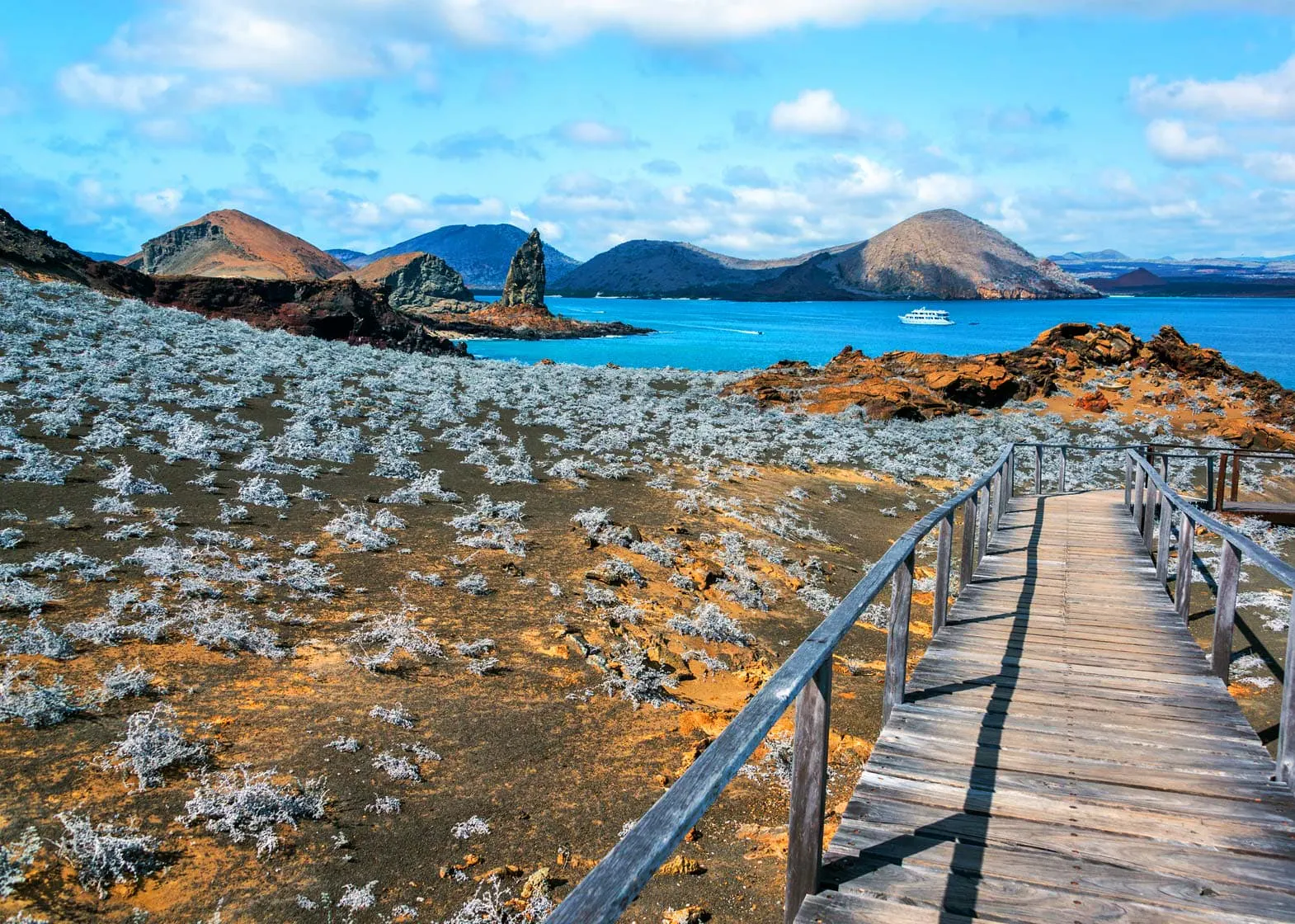 Explore the Galapagos Islands: A wooden walkway leading to a beach with mountains in the background.