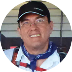A man with a backpack and hat smiles for the camera.