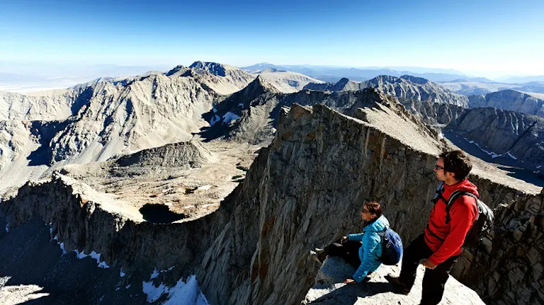 Two people experiencing the best hikes of a lifetime on the edge of a mountain.