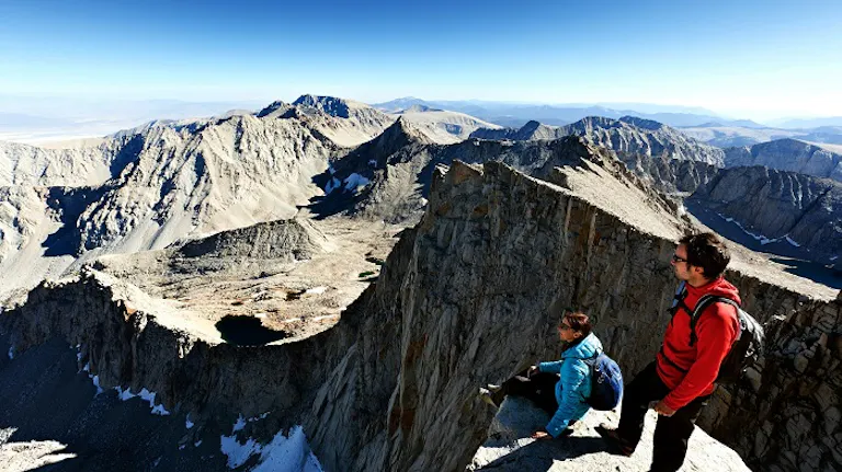 Two people experiencing the best hikes of a lifetime on the edge of a mountain.