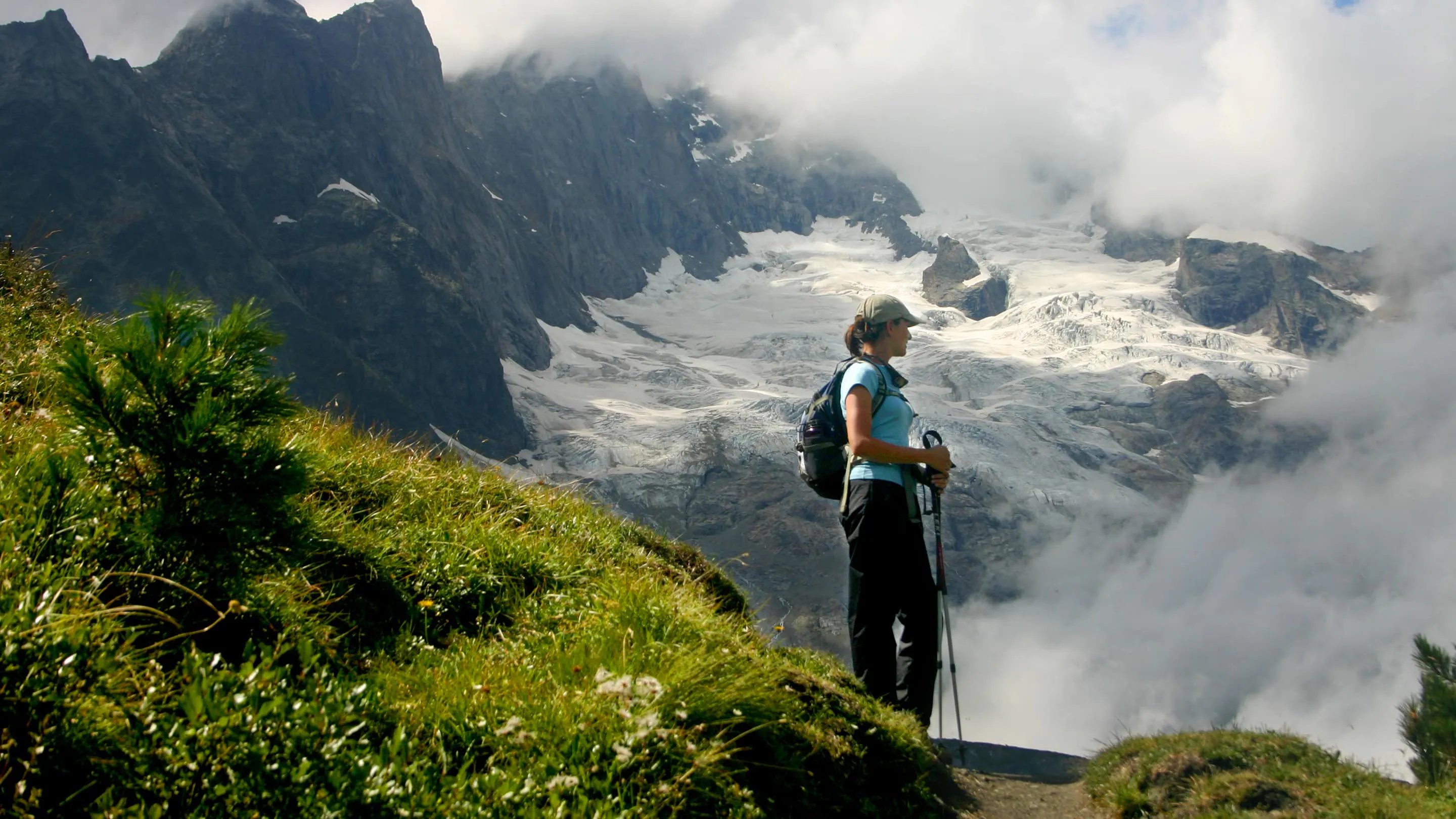 A man is standing on a path near a mountain with clouds in the background, offering one of the best hikes of a lifetime.