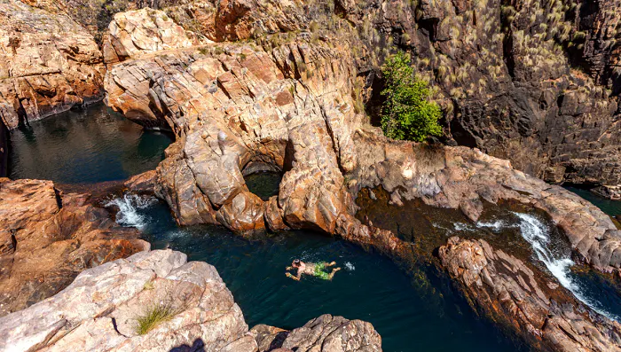 A man is floating in the water near a rocky cliff at Kakadu National Park, Australia.
