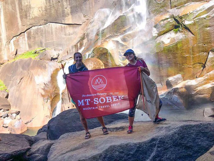 Two people practicing responsible tourism by standing in front of a waterfall holding a red banner.