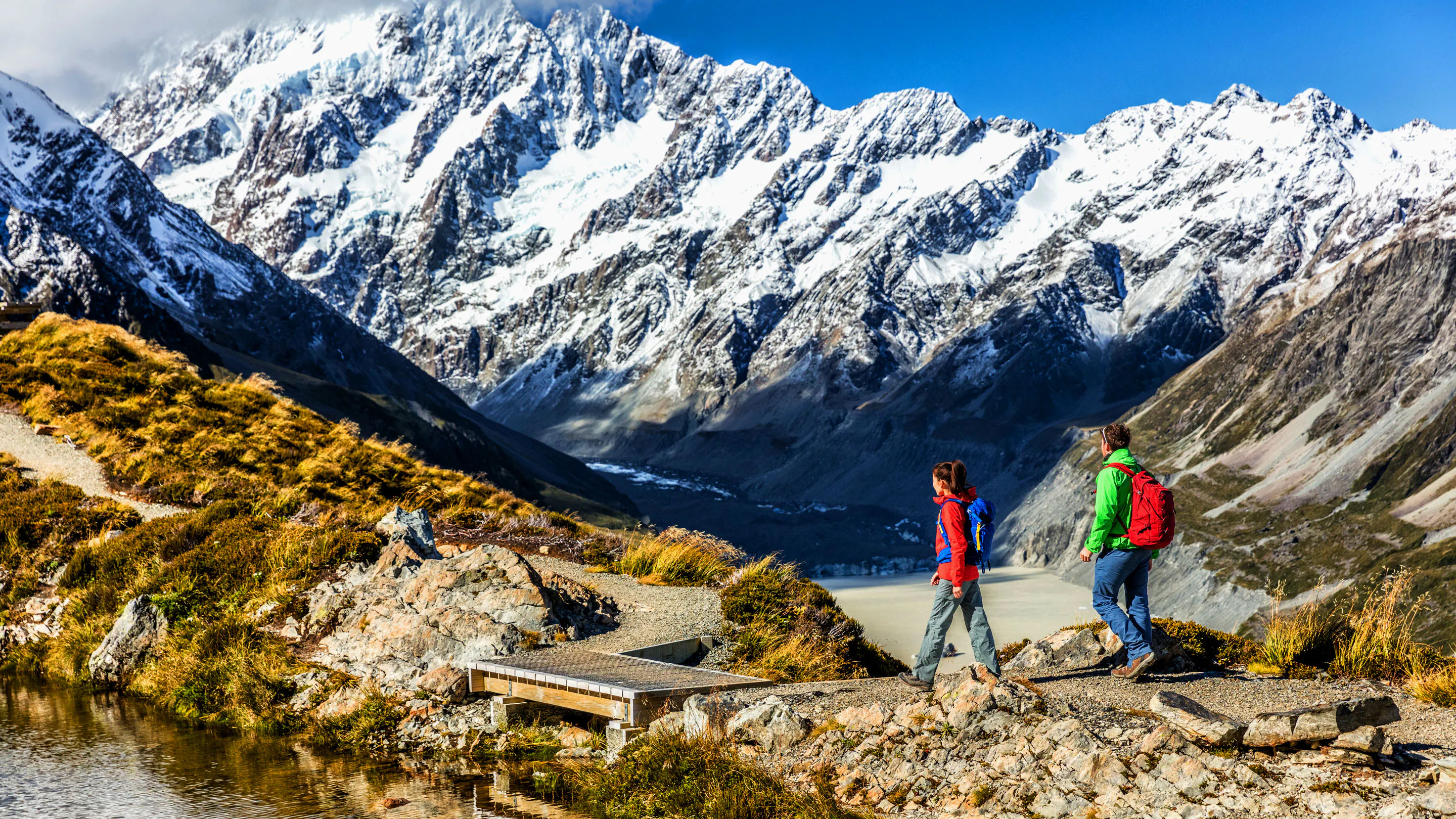 Two people hiking in New Zealand with beautiful snow capped mountains in the background