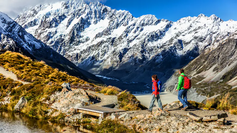 Two people hiking in New Zealand with beautiful snow capped mountains in the background