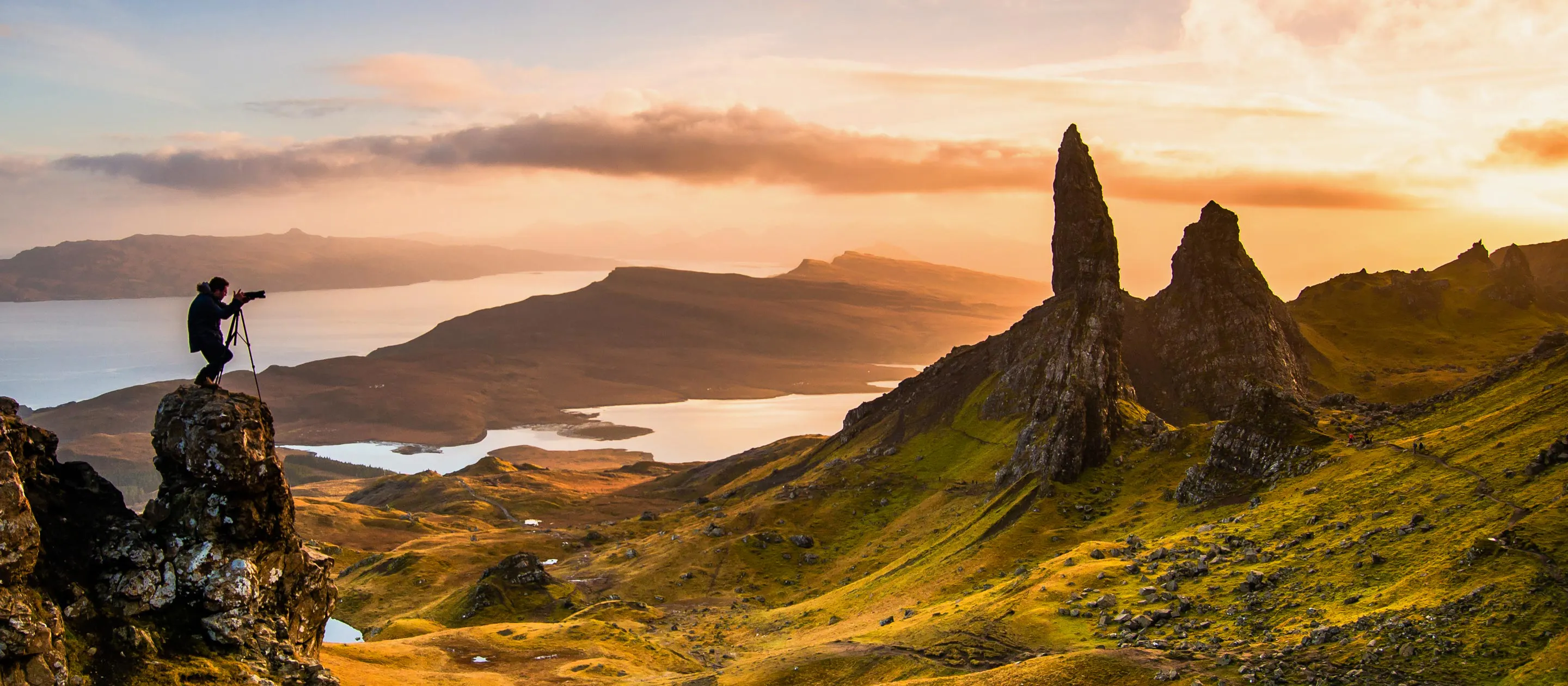 A person practicing sustainable travel standing on top of a cliff overlooking a lake in Scotland.