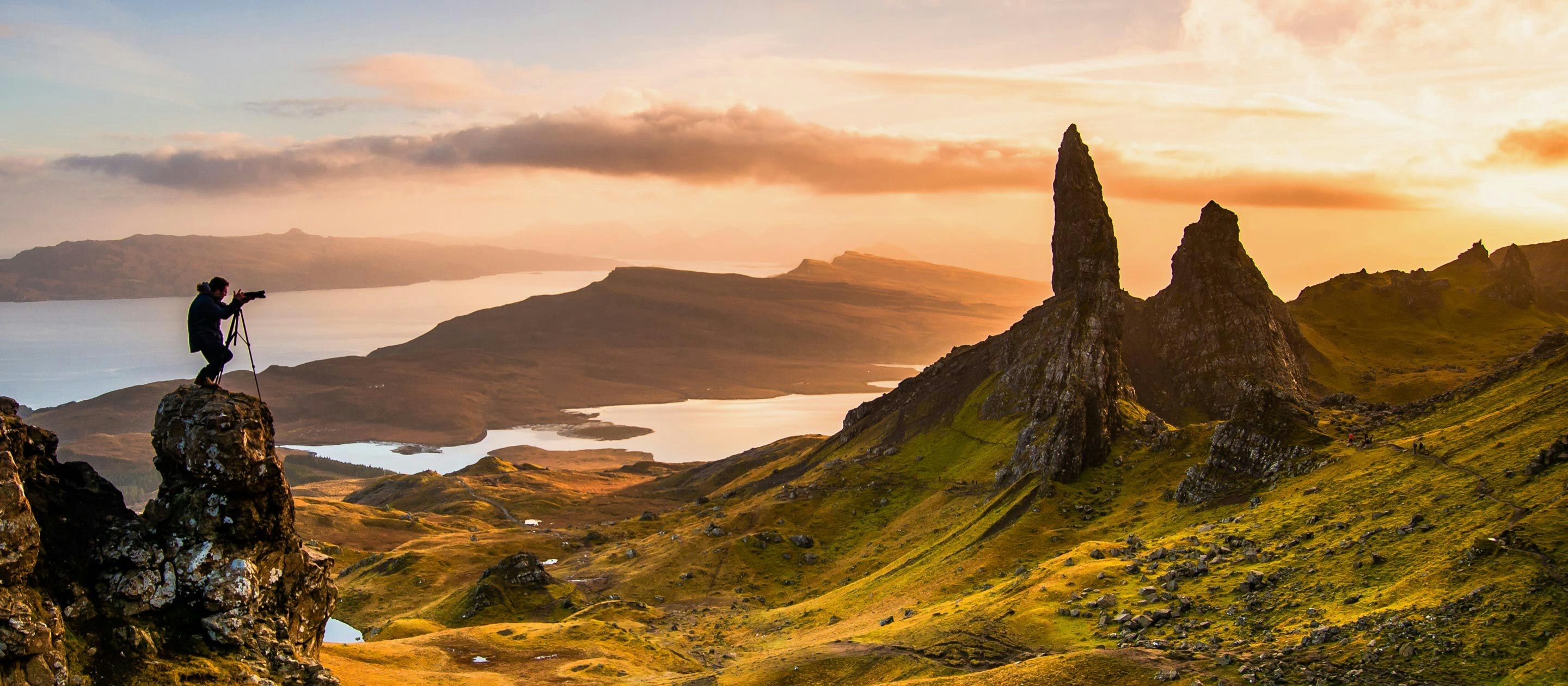 A person practicing sustainable travel standing on top of a cliff overlooking a lake in Scotland.