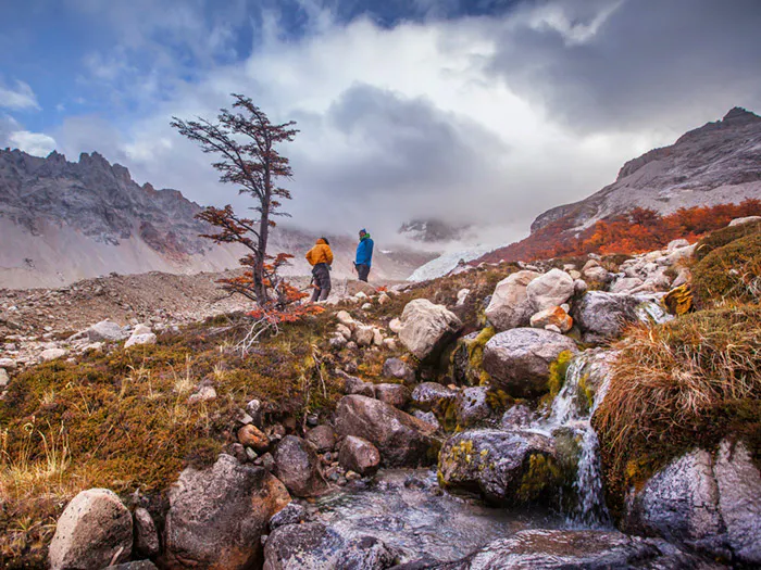 Two people practicing responsible tourism next to a stream in the mountains.