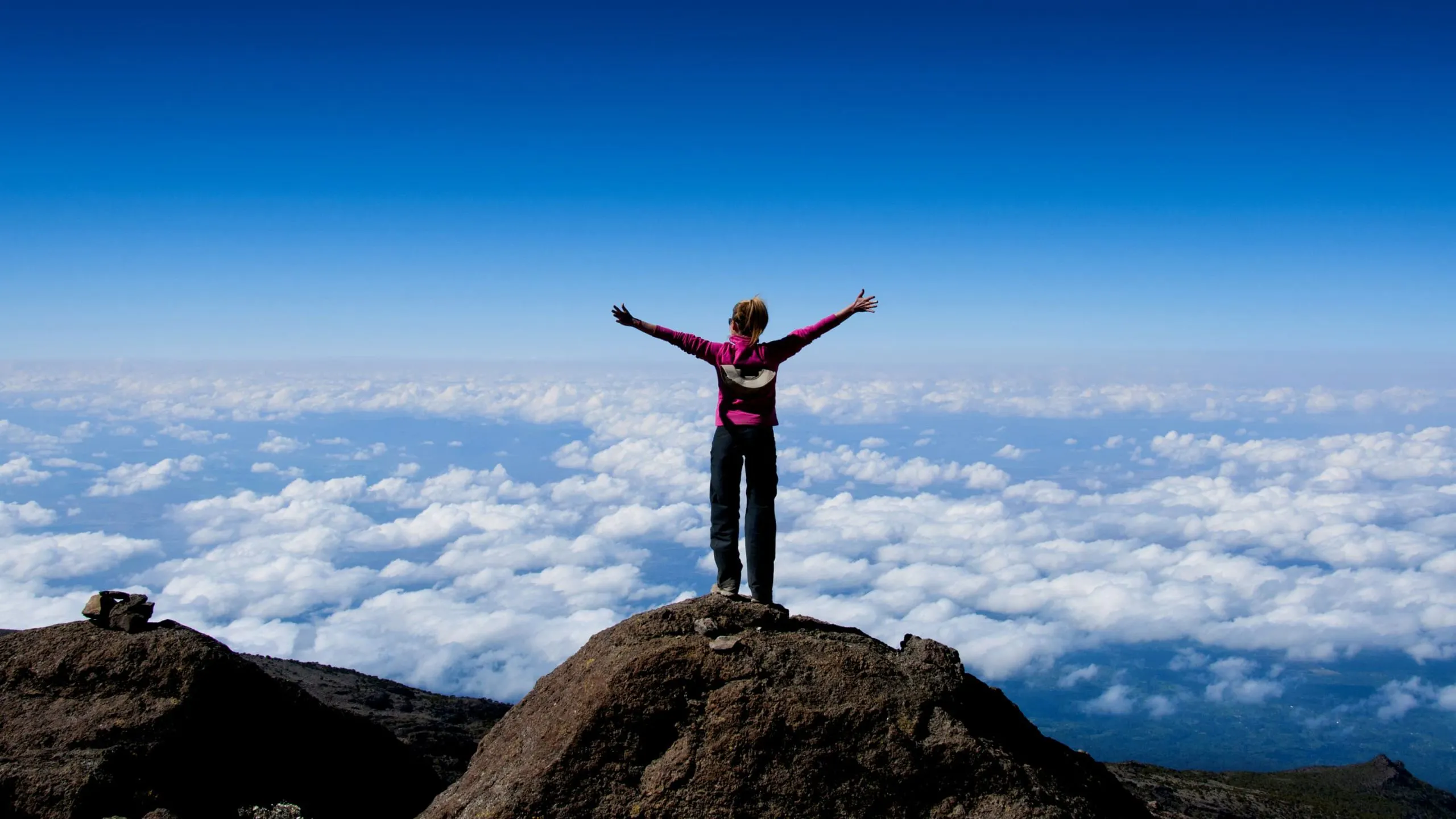 A person enjoying the health benefits of standing on top of a mountain with arms outstretched.