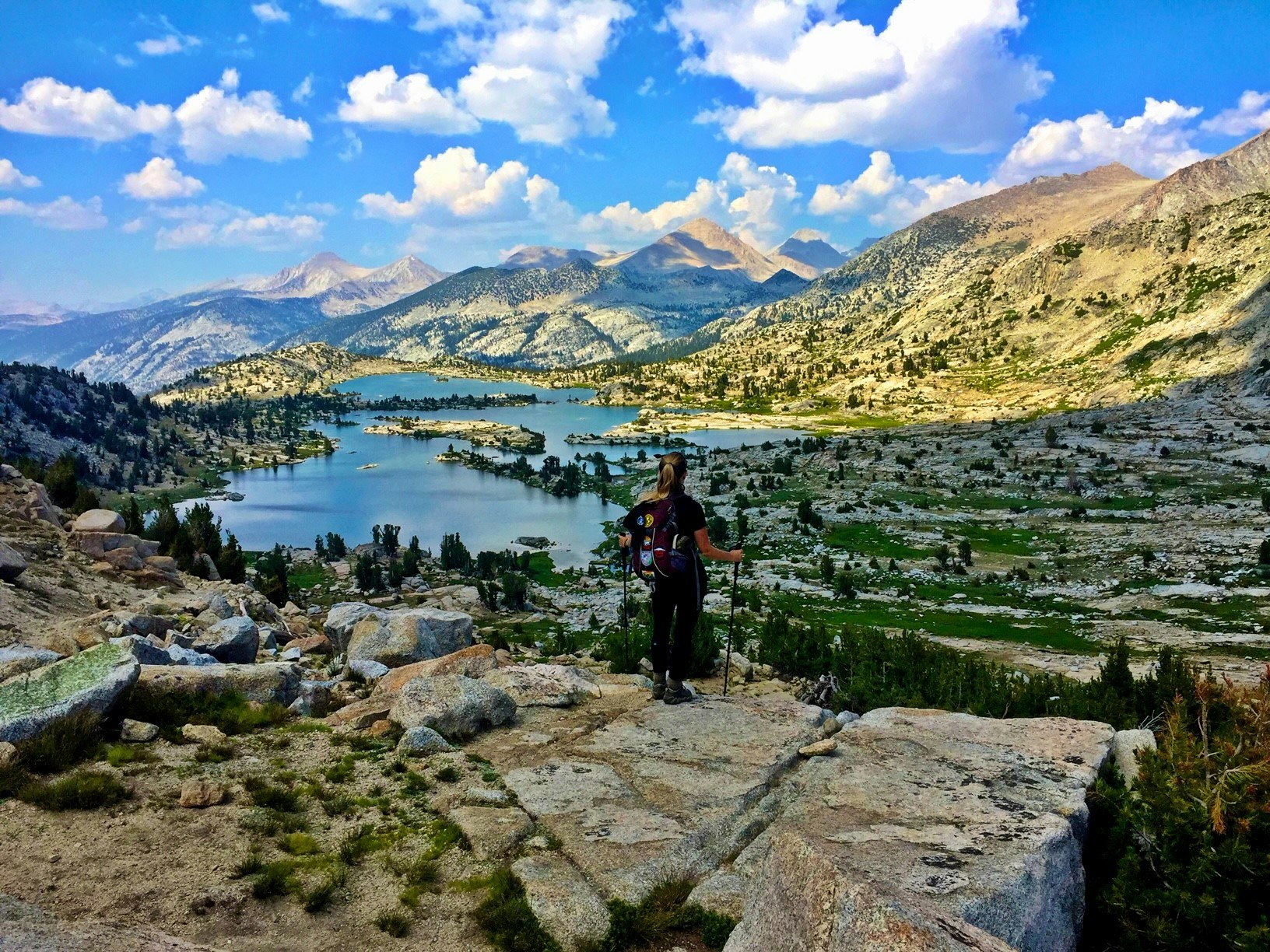 A hiker standing on top of a rocky mountain overlooking a lake.