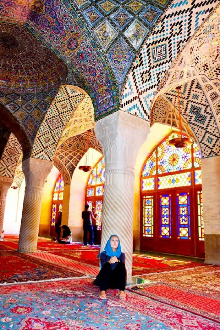 A woman sits on a rug inside a mosque.