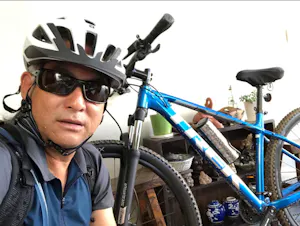 A man wearing a helmet and sunglasses takes a selfie with his bike.
