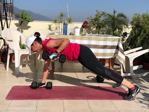 A woman doing a push up with dumbbells on a patio.