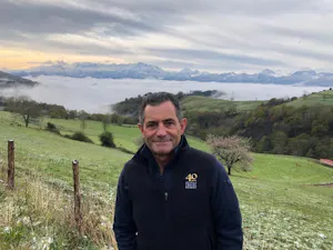 A man standing in front of a field with mountains in the background.