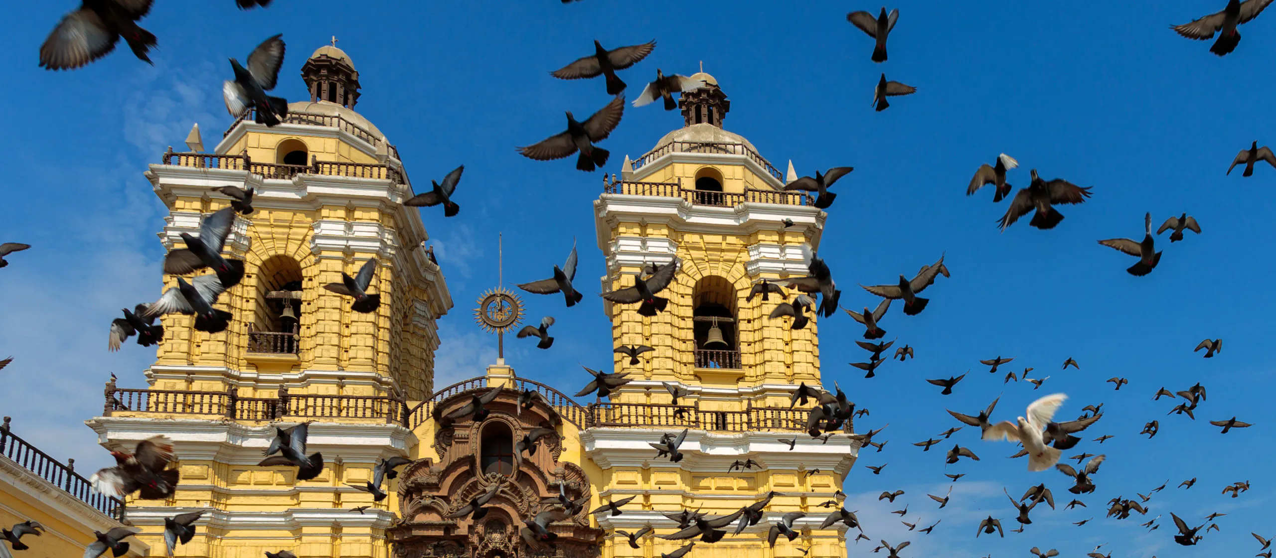 Pigeons flying in front of a yellow church.
