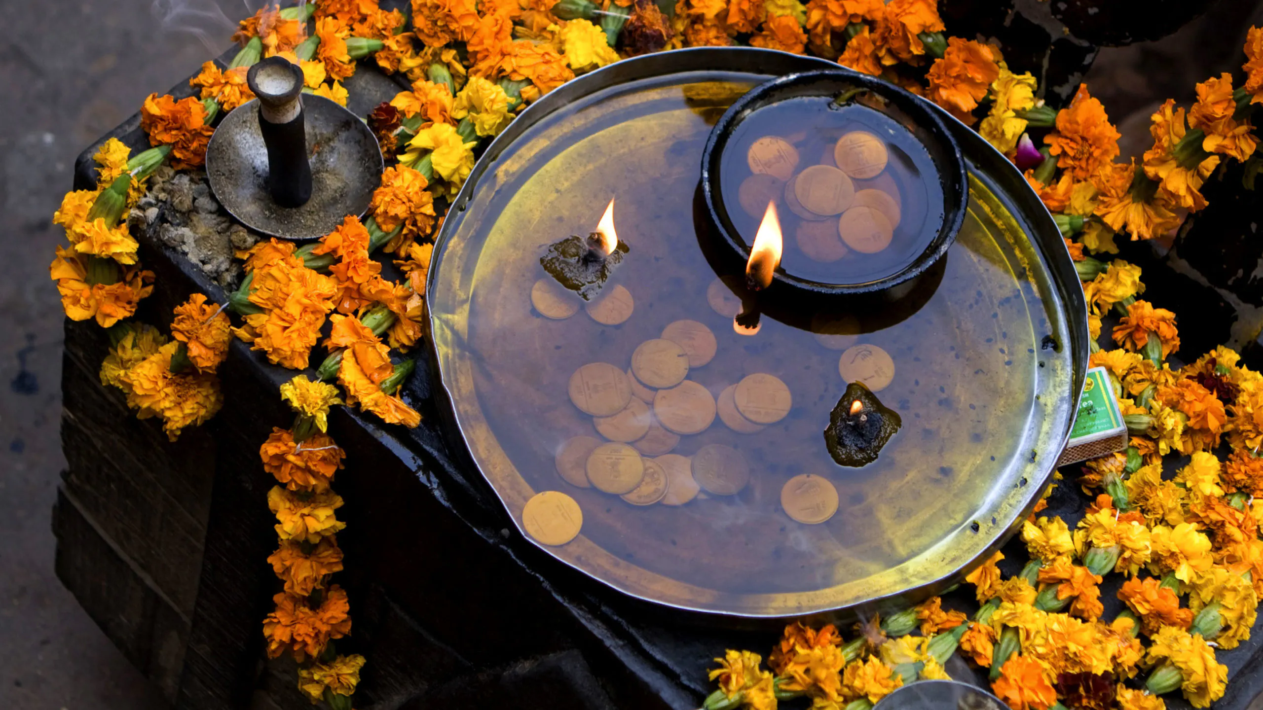 A bowl filled with flowers and candles in front of a temple.