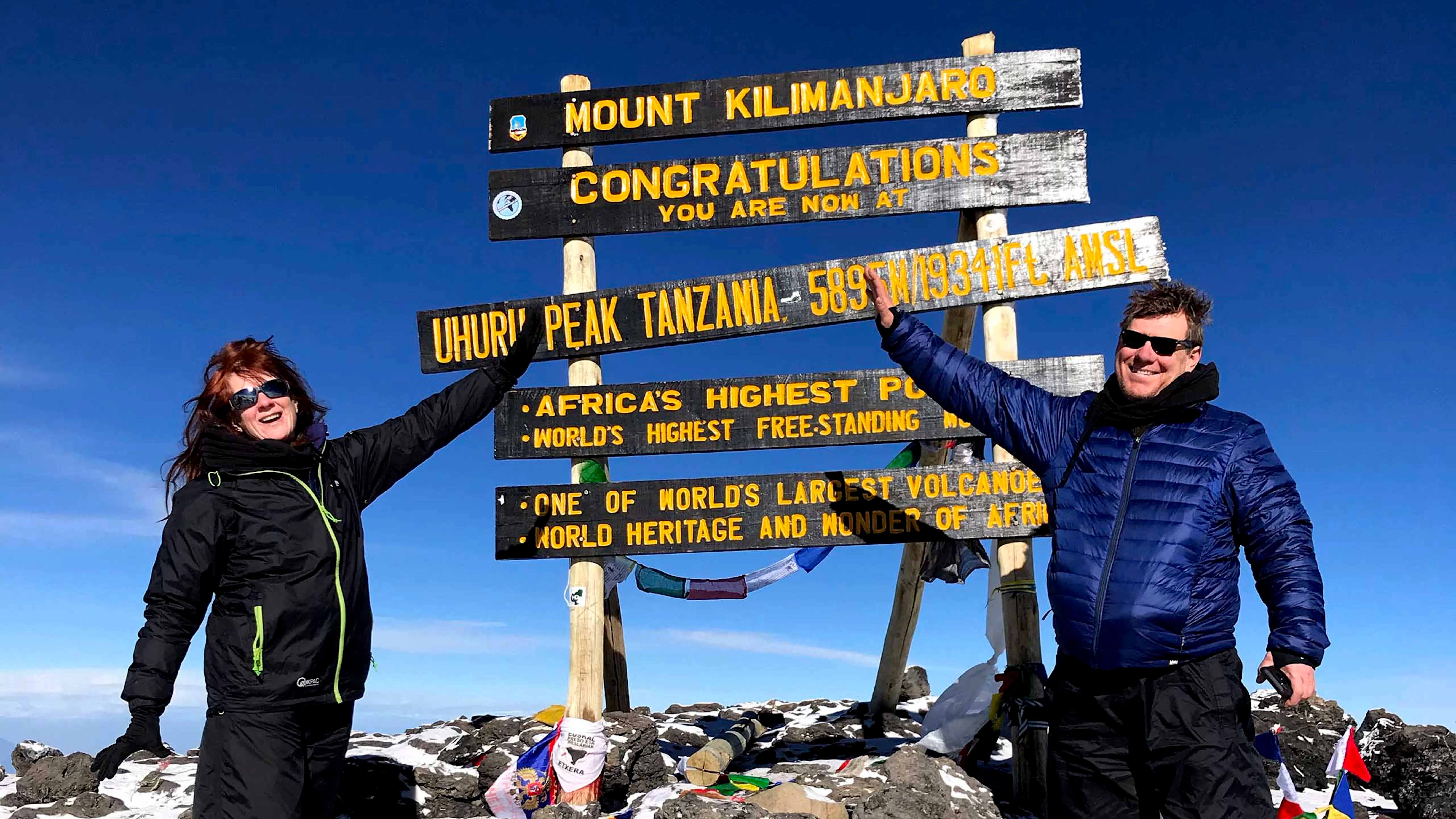 Two people standing in front of a sign at the summit of Mt. Kilimanjaro, representing adventure travel.