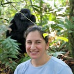 A woman smiles in front of a gorilla in the forest during an adventure.