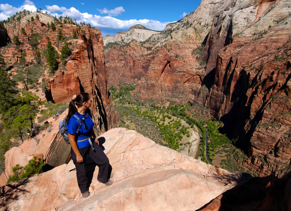 A woman standing on a rocky cliff overlooking a canyon in Utah national parks.