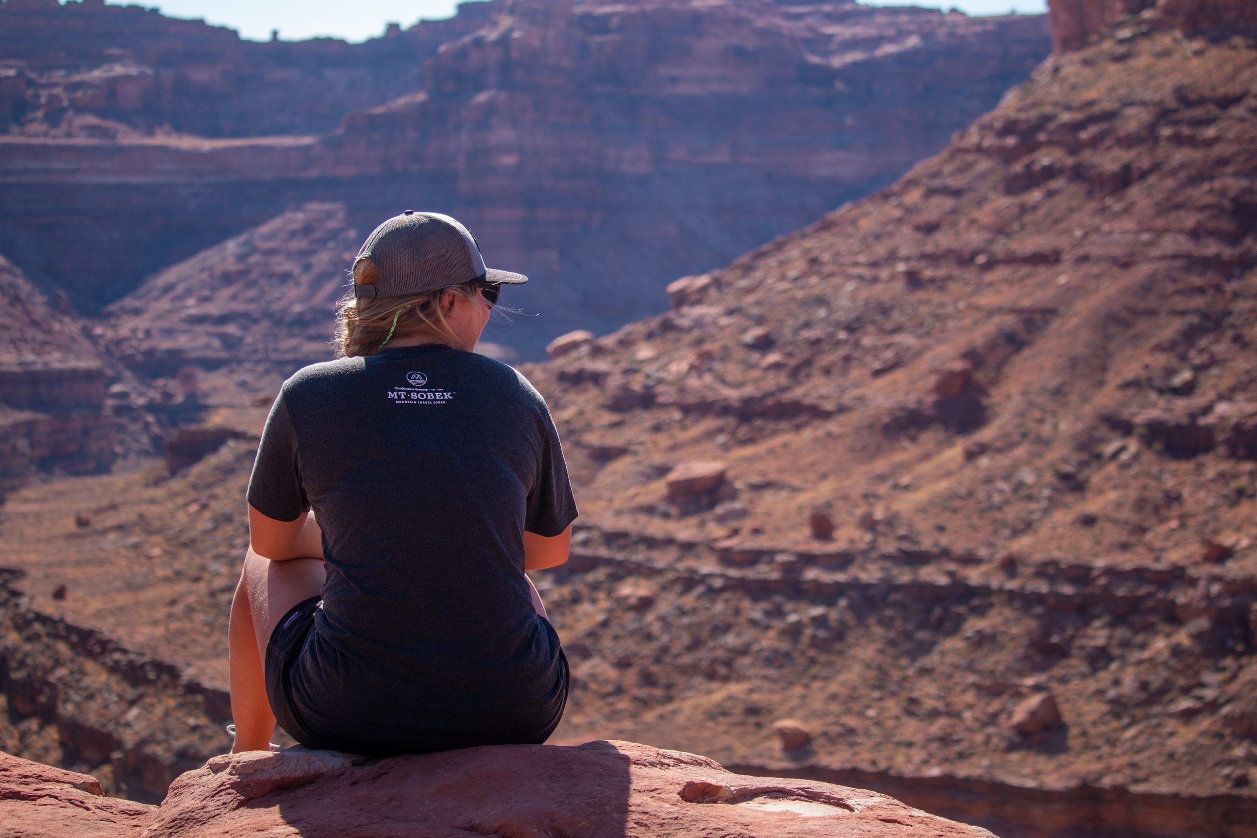 A woman sitting on a rock overlooking a canyon, offering T-Shirts & Gifts.