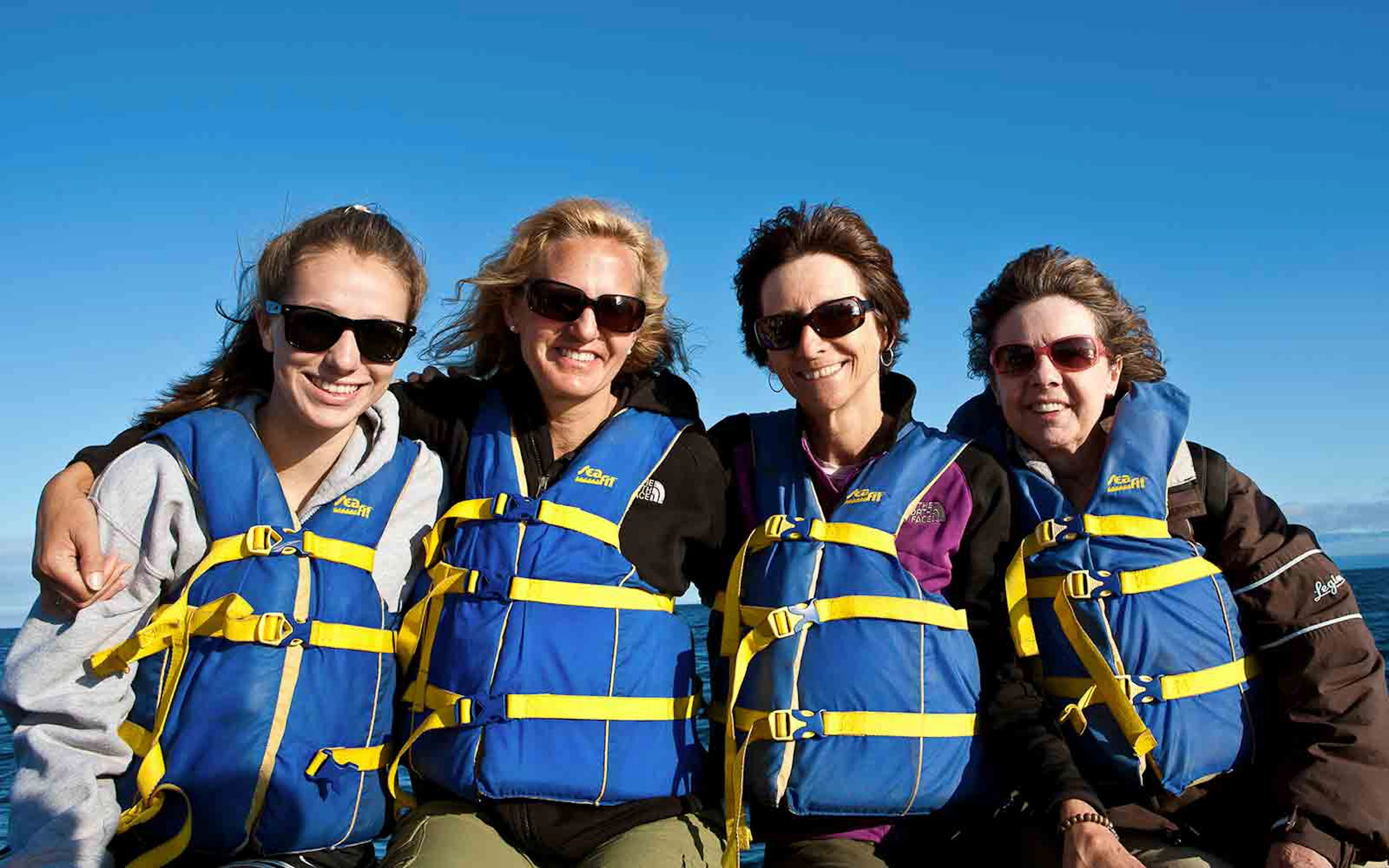 Four women wearing life jackets on a boat.