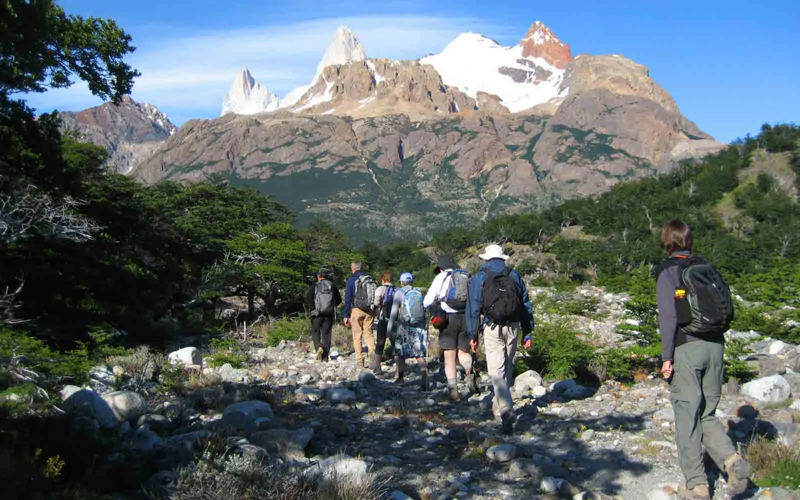 A group of people hiking on a trail with mountains in the background.