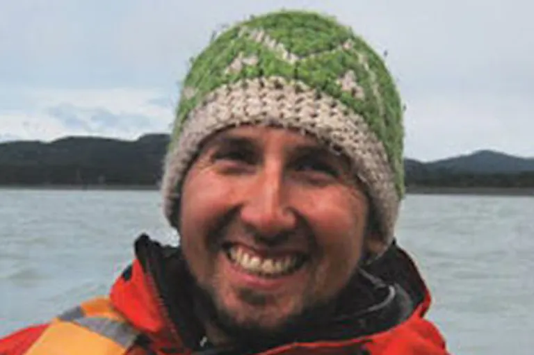 A smiling man wearing a knitted hat on a boat.