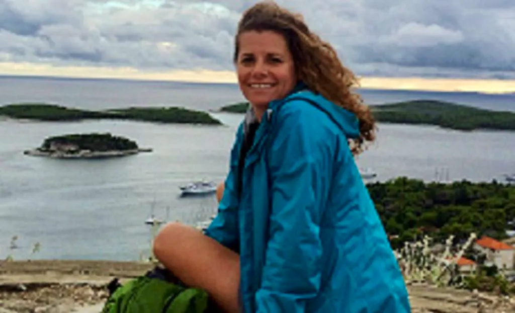 A woman in a blue jacket sitting on top of a mountain.