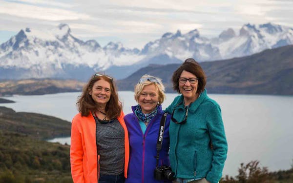 Three women standing in front of a lake with mountains in the background.