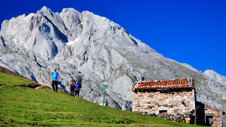 Two people standing on a grassy hill next to a mountain.