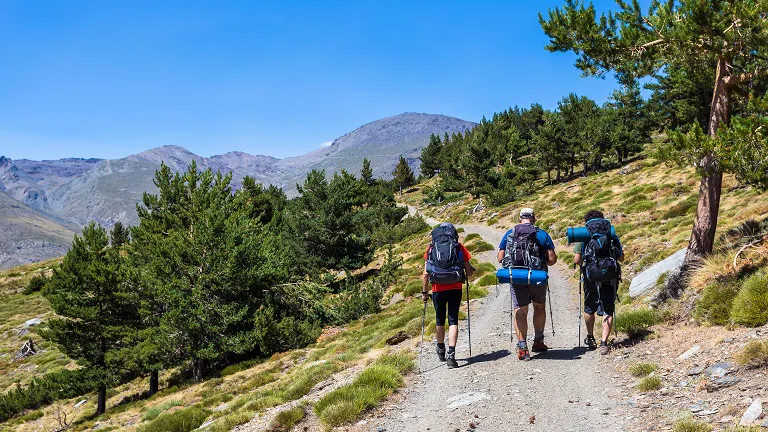 Three people hiking on a trail in the mountains.