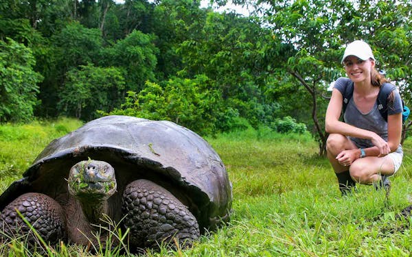 A woman kneeling down next to a giant tortoise.